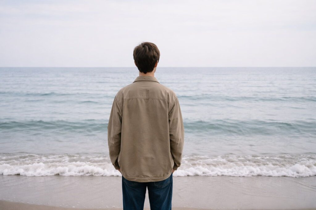 a person standing by the ocean, looking toward the horizon in a moment of uncertainty