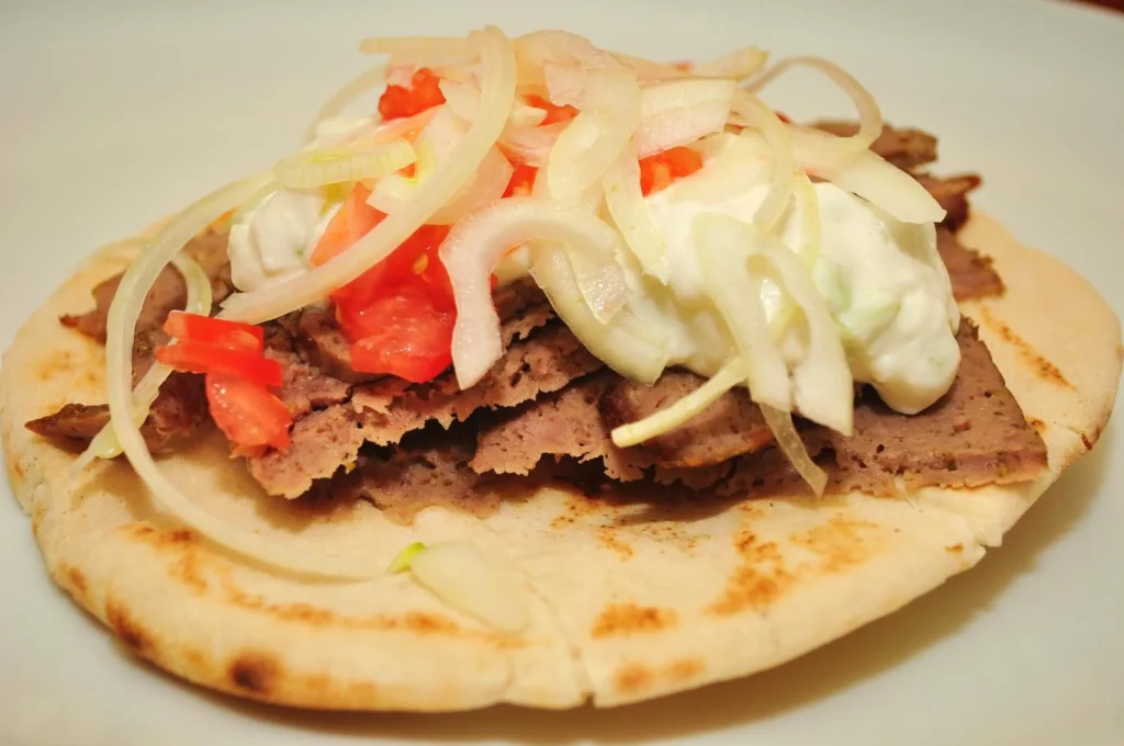 gyro meat served on pita bread with onions tomato and yogurt sauce